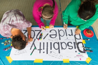 Three people painting a Disability Pride sign