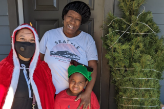 A smiling family of three receiving a bundled Christmas tree at their front door