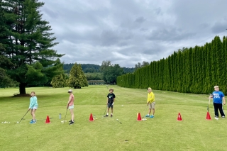Five kids on a golf course holding their clubs and about to practice hitting some balls