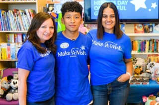 Two adults and a teenager wearing blue Make-A-Wish t-shirts with bookshelves in the background