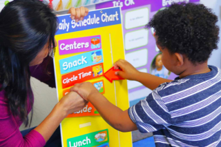 An adult with a child playing with a Daily Schedule Chart