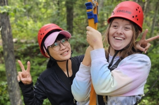 Two people wearing helmets strapped in for a zipline ride