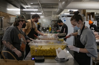 Four people in a kitchen scooping food into take-away boxes