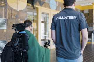 A volunteer for ALS Northwest walking beside a man in a wheelchair