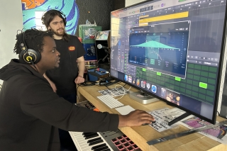 Two people in a recording studio producing music and looking a very large monitor