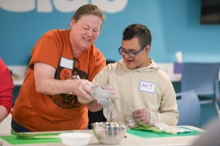 An adult helping a teenager cooking in a kitchen