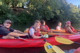 Several adults and teens on the river in double kayaks