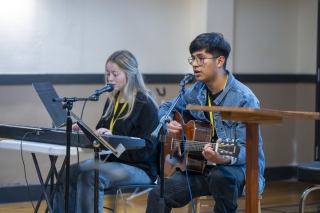 Two young people performing on stage, one on the keyboards and one with a guitar