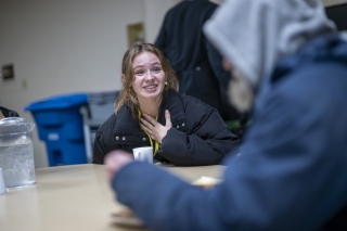 A young volunteer with Portland Rescue Mission sitting at a table and talking with someone