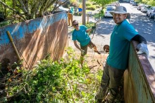 Two volunteers loading tree branches into a large yard debris dumpster