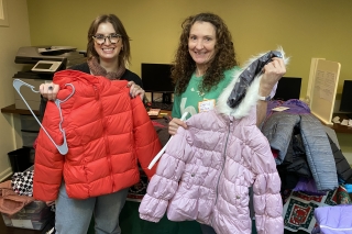 Two volunteers holding up two colorful jackets while sorting through clothes