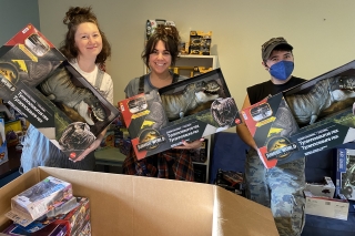 Three volunteers holding up three toy Tyrannosaurus Rex