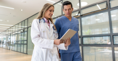 A female and male doctor looking at a tablet while walking