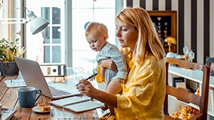 A mother holding her child and working on her laptop